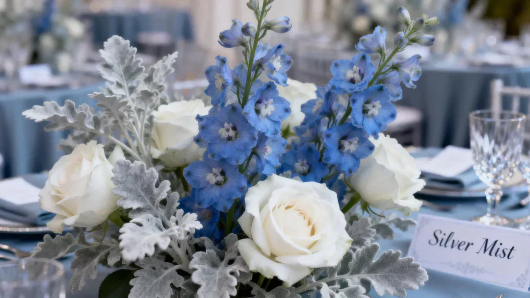 A cinematic, high-fashion wedding photography shot of a bridal bouquet featuring dusty blue delphiniums, white O'Hara roses, and silver dusty miller foliage