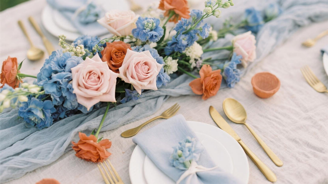Dusty blue wedding flowers, blush roses, terracotta accents, gold cutlery on linen table