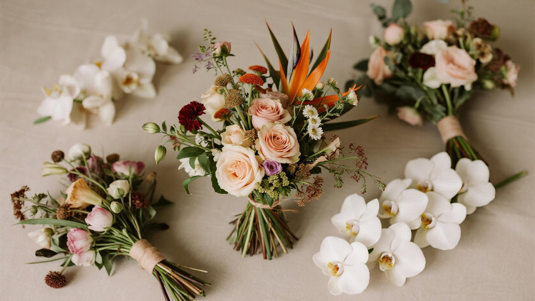 Modern flat lay of assorted wedding flower arrangements with roses and orchids on beige fabric