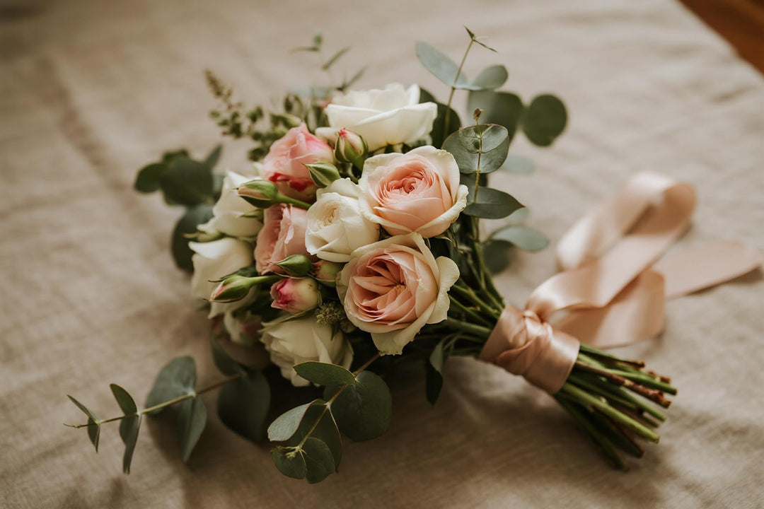Romantic wedding flower bouquet with pink and white roses, eucalyptus, and ribbon on linen.
