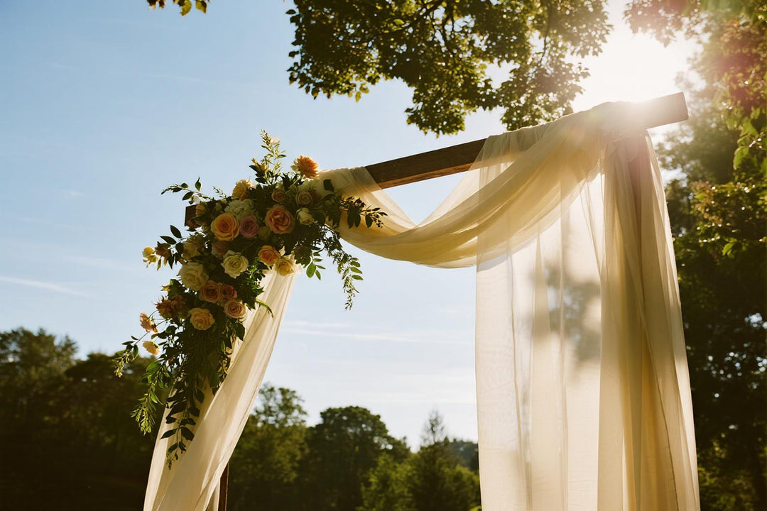 Outdoor wedding ceremony arch with sheer fabric, greenery, and pastel floral arrangements
