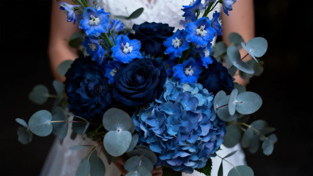 A stunning, high-resolution close-up of a bridal bouquet featuring a mix of electric blue Delphiniums, deep Navy Hydrangeas, and Dusty Blue Eucalyptus