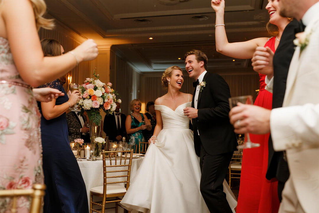 Elegant modern wedding reception with bride and groom laughing, gold chairs, floral centerpieces