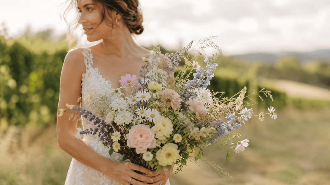 Bride holding a loose and romantic wildflower bridal bouquet with pastel meadow flowers in an outdoor wedding setting