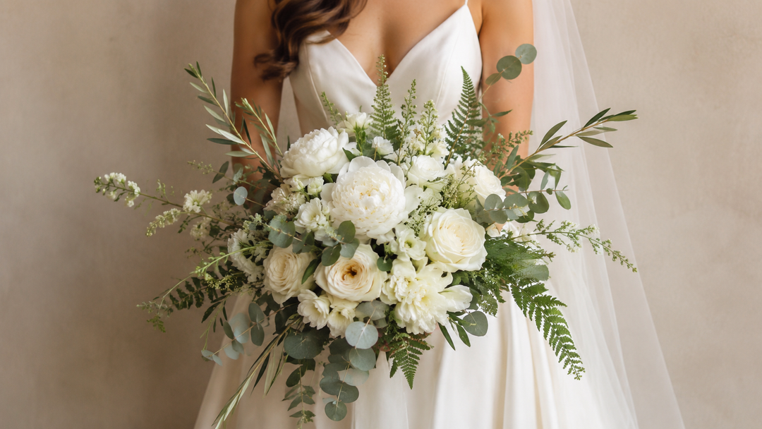 Bride holding an elegant white and green bridal bouquet with layered white flowers and mixed greenery in soft natural light.