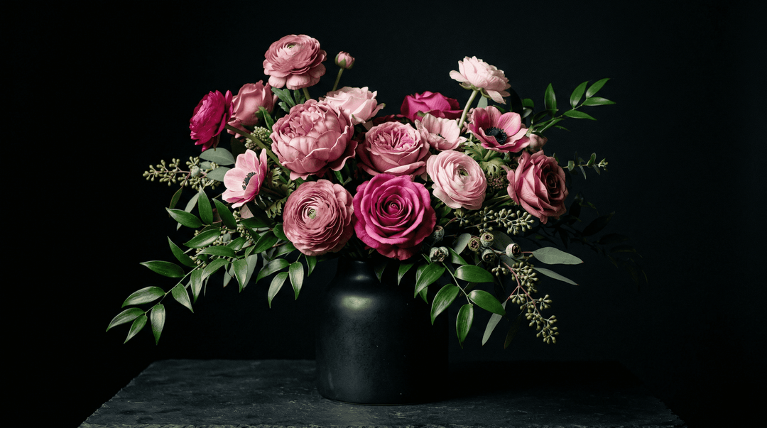 Editorial close-up of a modern structural bouquet in dusty rose, magenta, and blush, blending realistic silk flowers with fresh Italian ruscus and seeded eucalyptus.