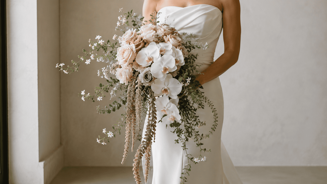 Luxury editorial shot of a cascading bouquet with white orchids, blush roses, carnations, trailing amaranthus, jasmine vine, and airy eucalyptus.