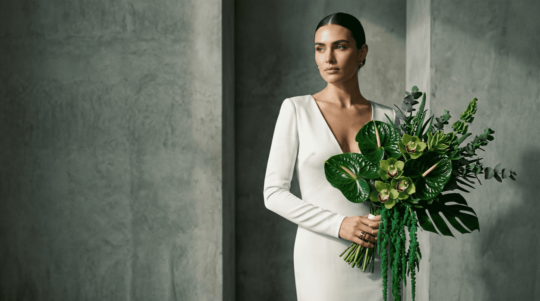 Photorealistic editorial wedding photography. A high-fashion bride in a sleek, minimalist ivory silk gown holding an architectural, fully green flower bouquet