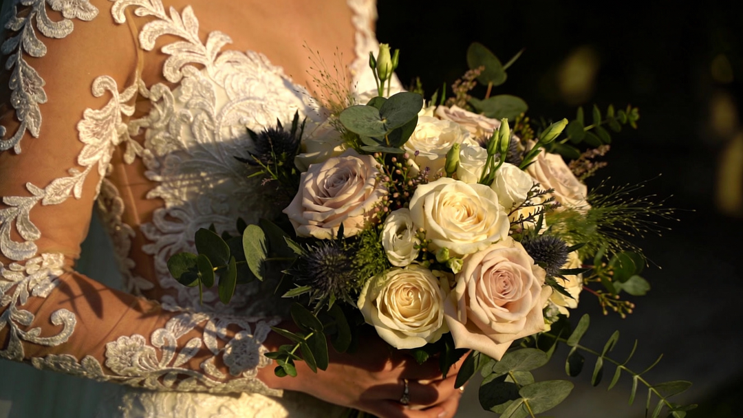 a sophisticated bride holding a stunning, texturally rich wedding bouquet. The bouquet features a mix of classic roses and wild, organic greenery, perfectly arranged